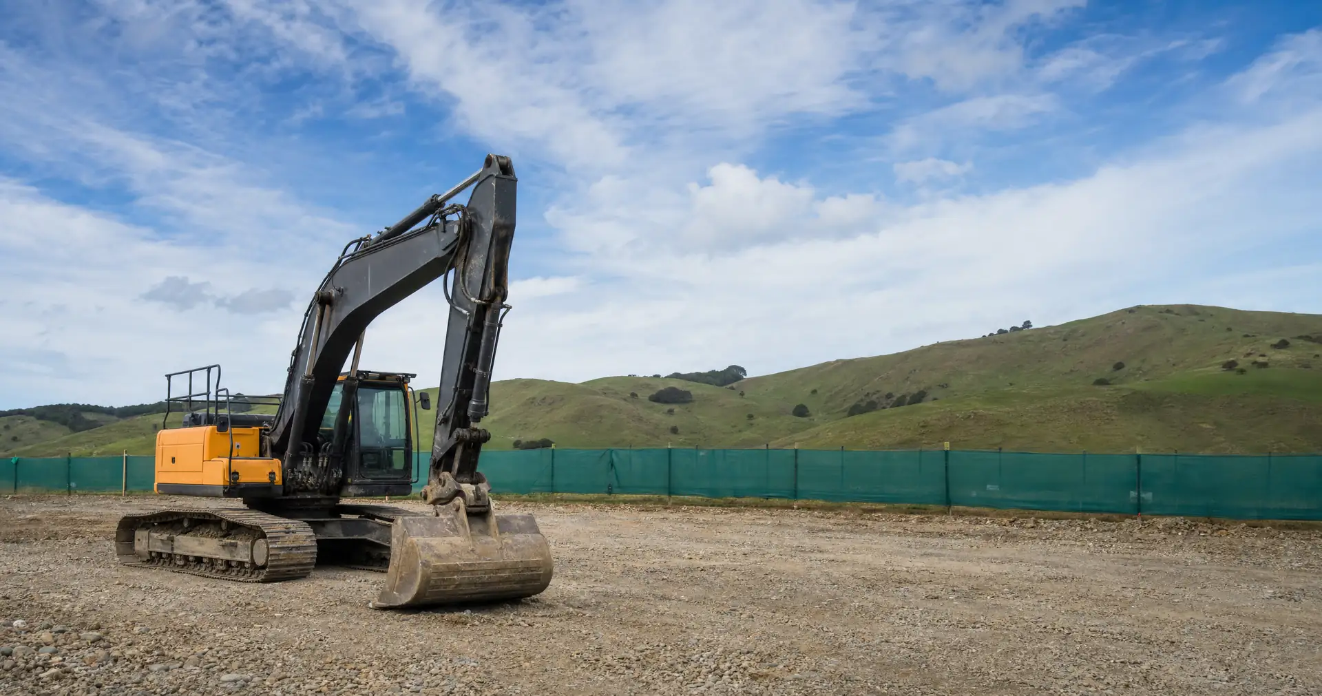 A tracked excavator with its bucket resting on cleared ground at an earthworks site