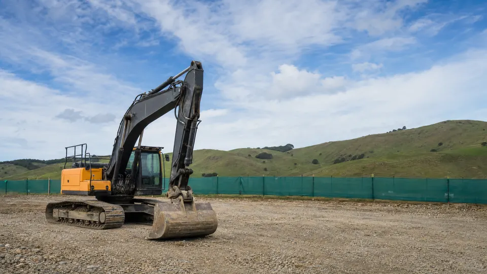 A tracked excavator with its bucket resting on cleared ground at an earthworks site