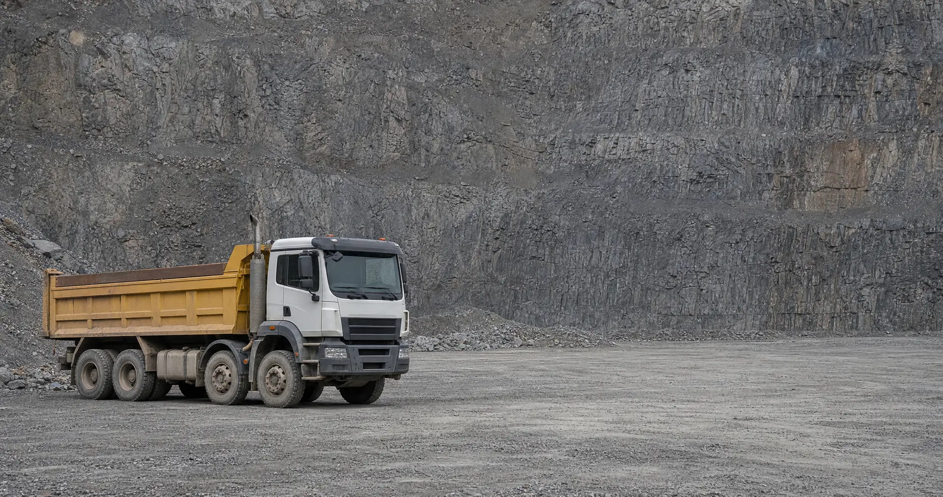 A heavy tipper truck parked on the floor of a working quarry below a rock face