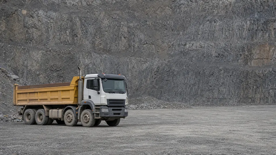 A heavy tipper truck parked on the floor of a working quarry below a rock face