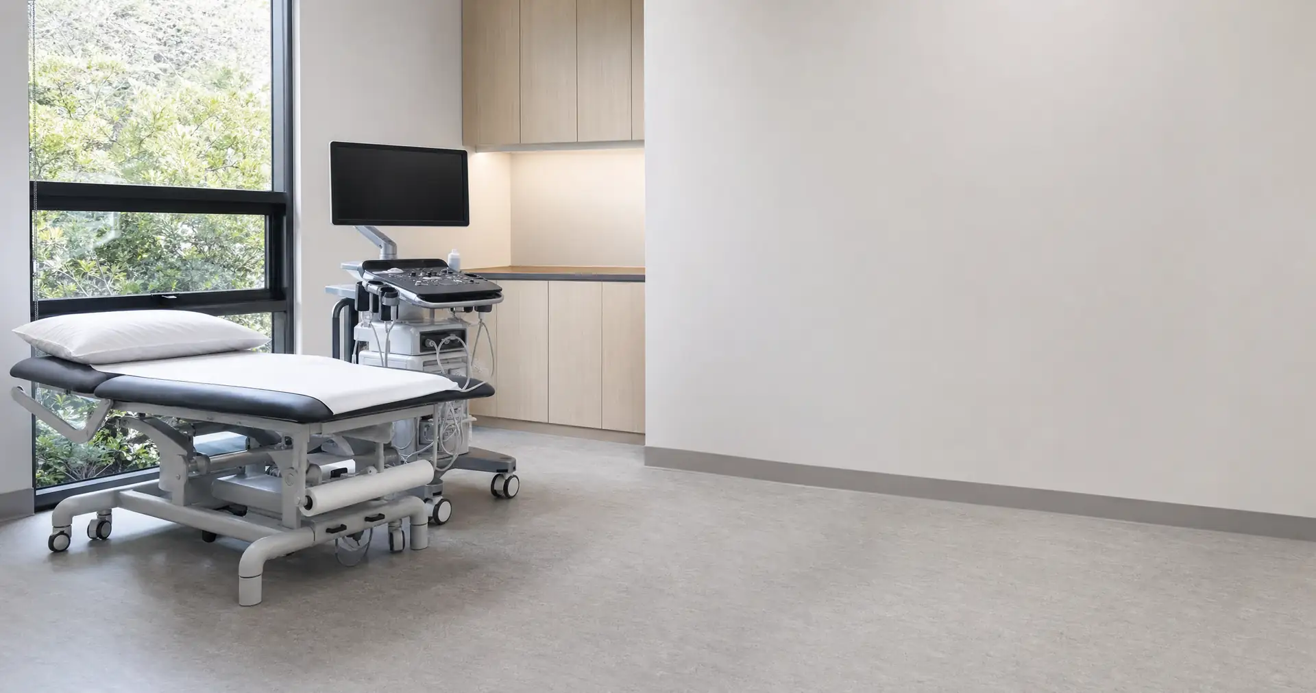 An examination couch and a mobile diagnostic cart in an empty clinical treatment room