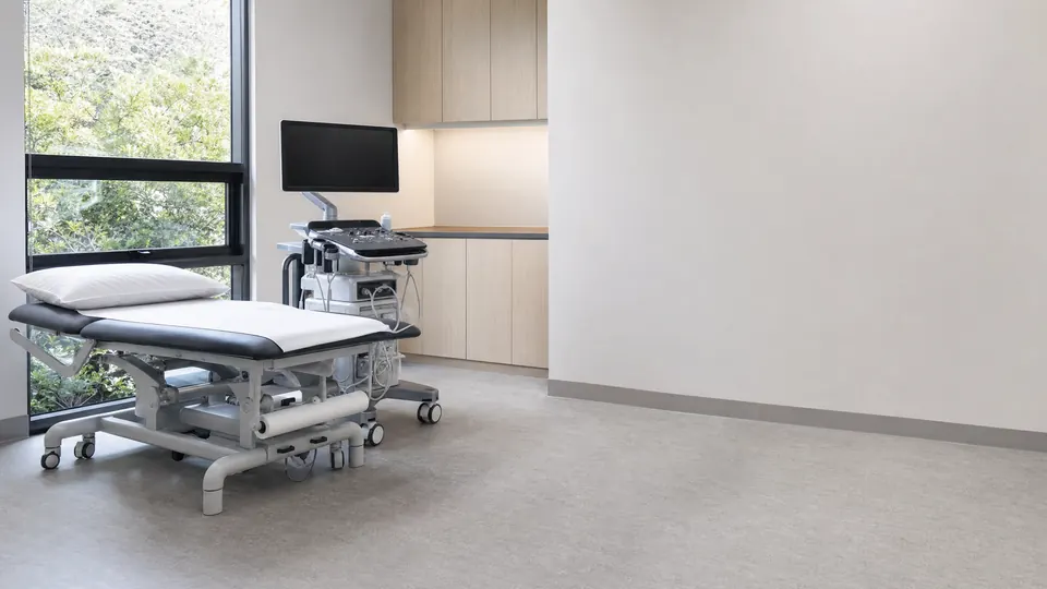 An examination couch and a mobile diagnostic cart in an empty clinical treatment room