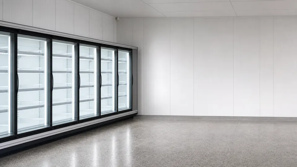 A run of empty glass-door commercial chiller cabinets along a cool store wall