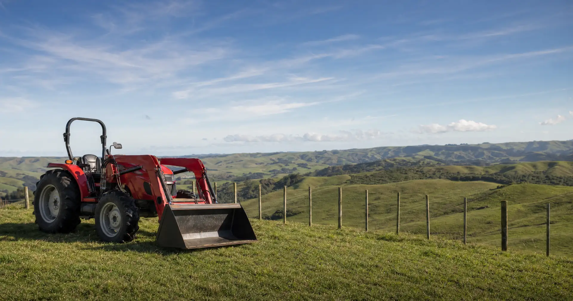 A farm tractor with a front loader parked on a grass headland beside a paddock