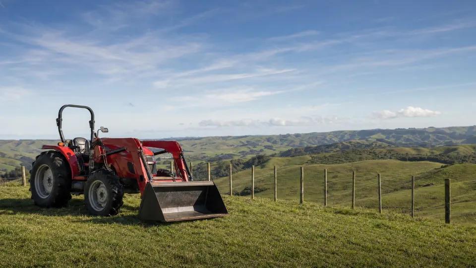 A farm tractor with a front loader parked on a grass headland beside a paddock