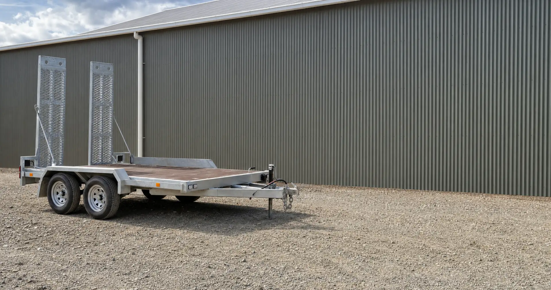 A tandem-axle flat-deck plant trailer parked on the gravel of a contractor yard
