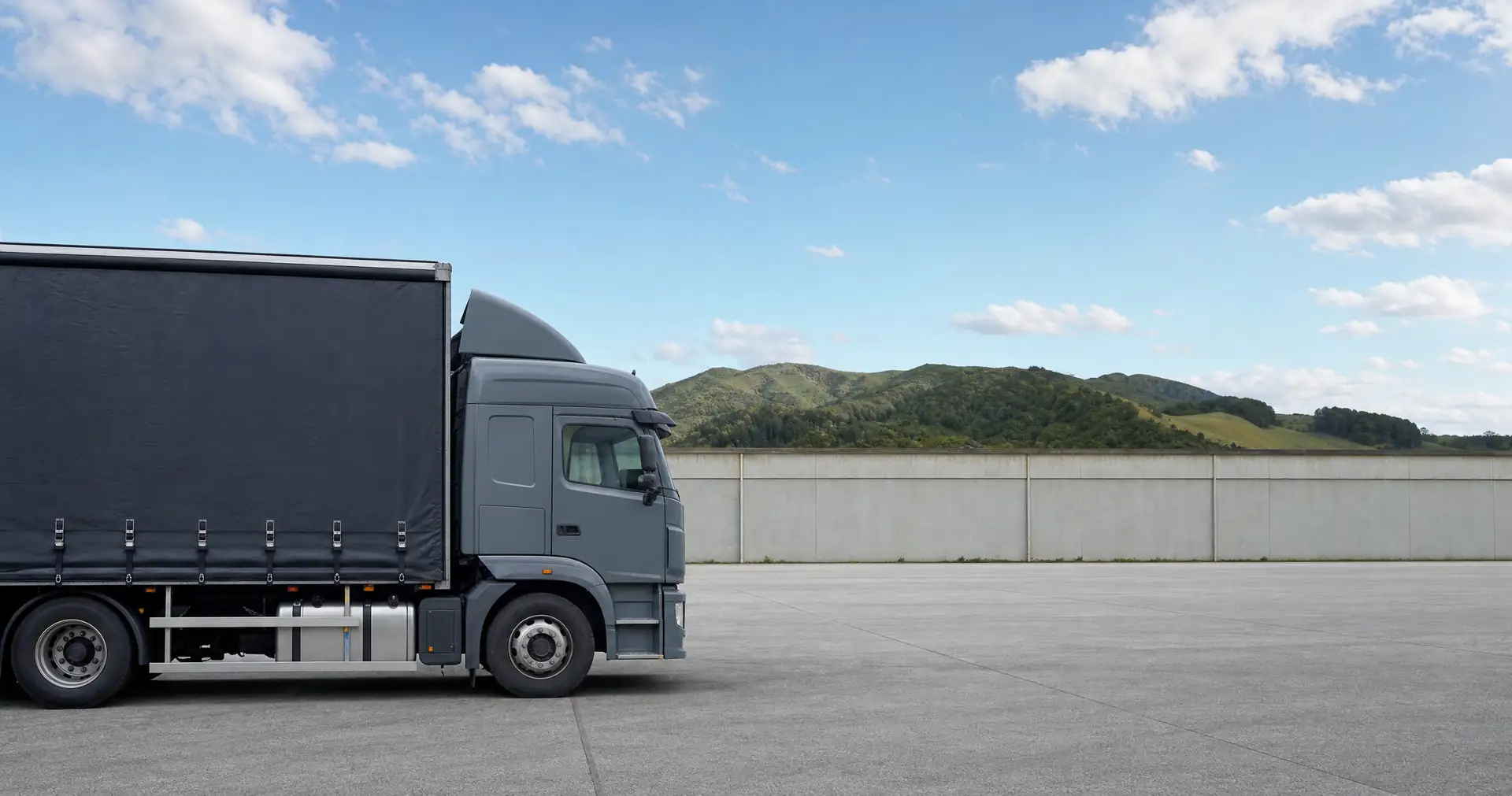 A curtainsider delivery truck parked side-on in a sealed freight yard
