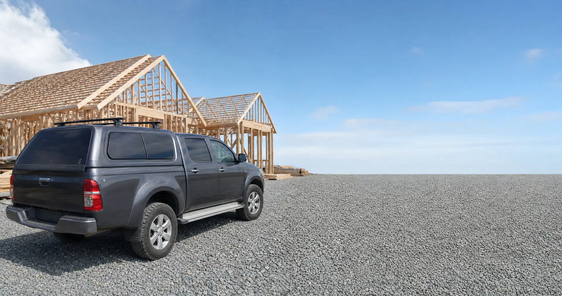 A double-cab ute with a canopy and roof rack parked at a residential building site