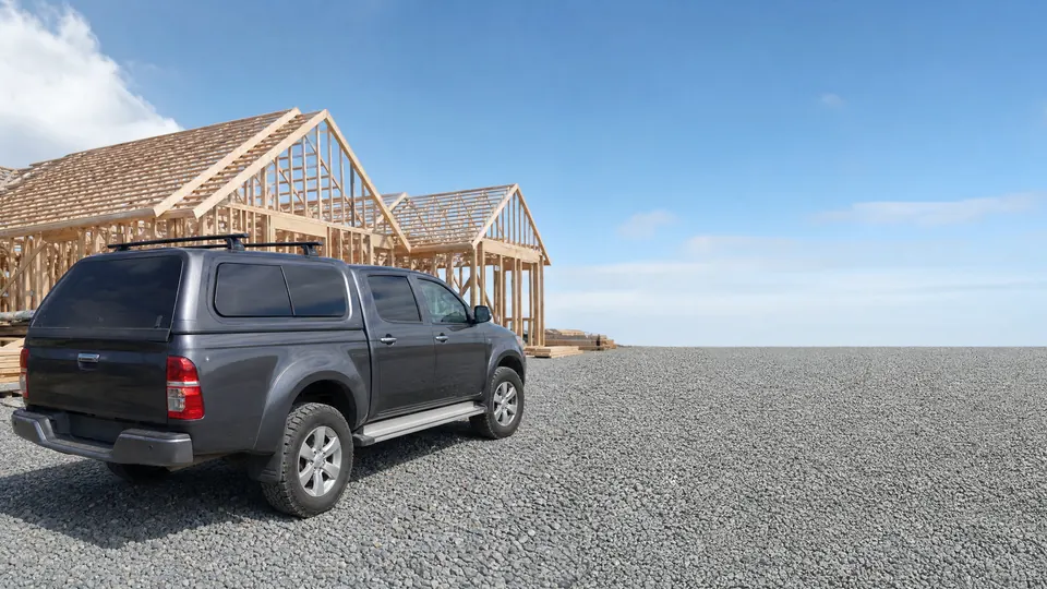 A double-cab ute with a canopy and roof rack parked at a residential building site