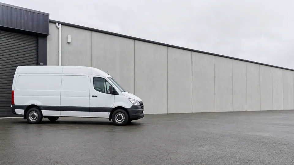 A plain white high-roof panel van parked on the forecourt of a light-industrial unit