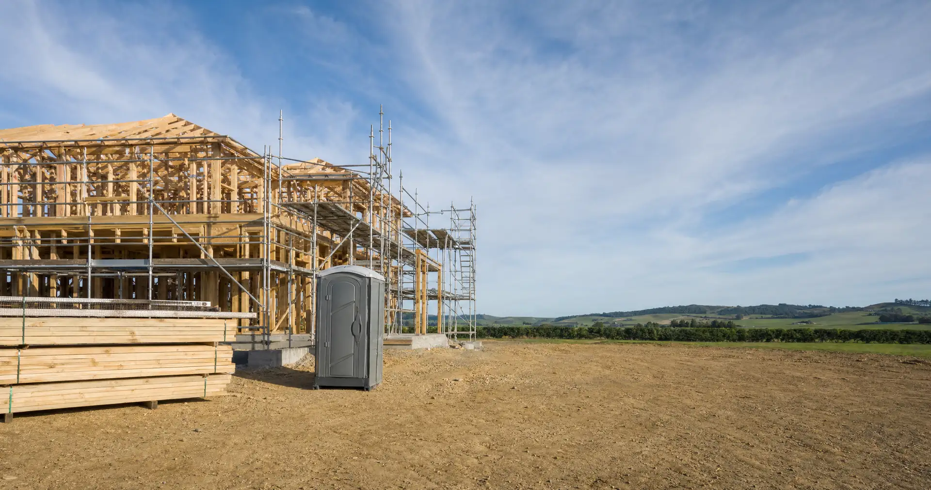 A partly framed two-storey timber house with scaffolding up one side on a cleared site