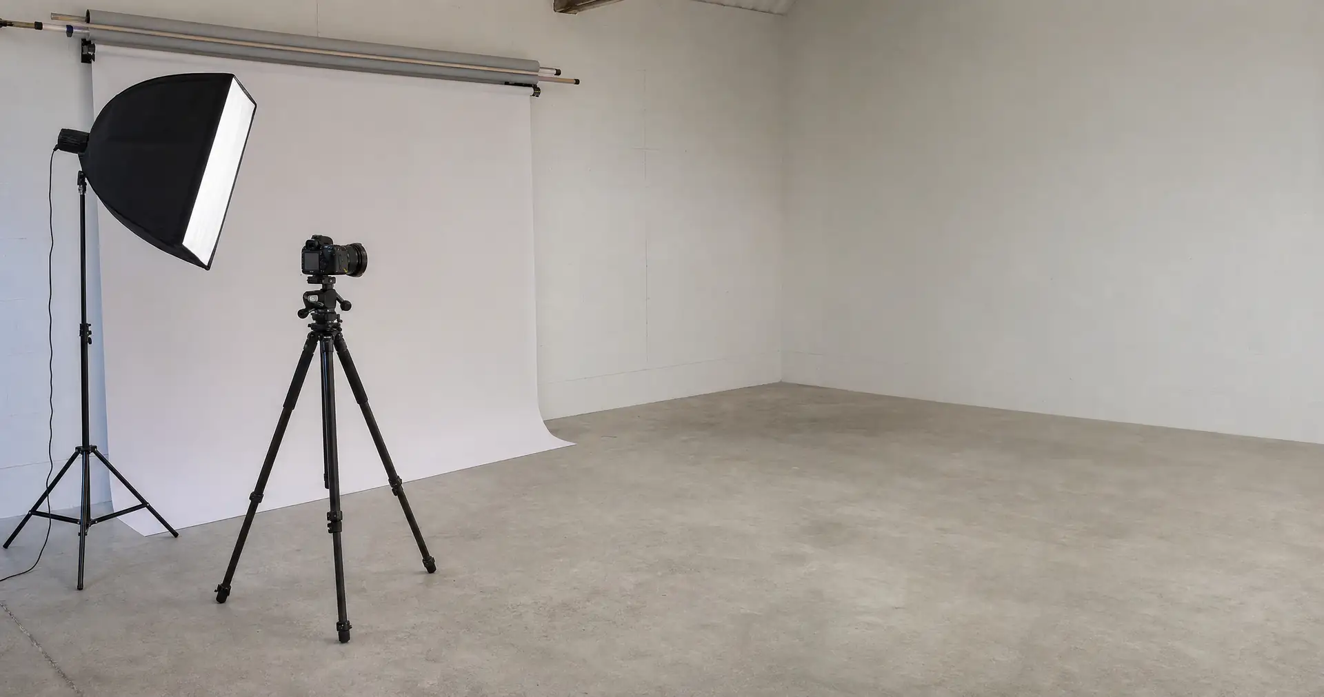 A camera on a tripod and a softbox light facing a paper backdrop in a small studio