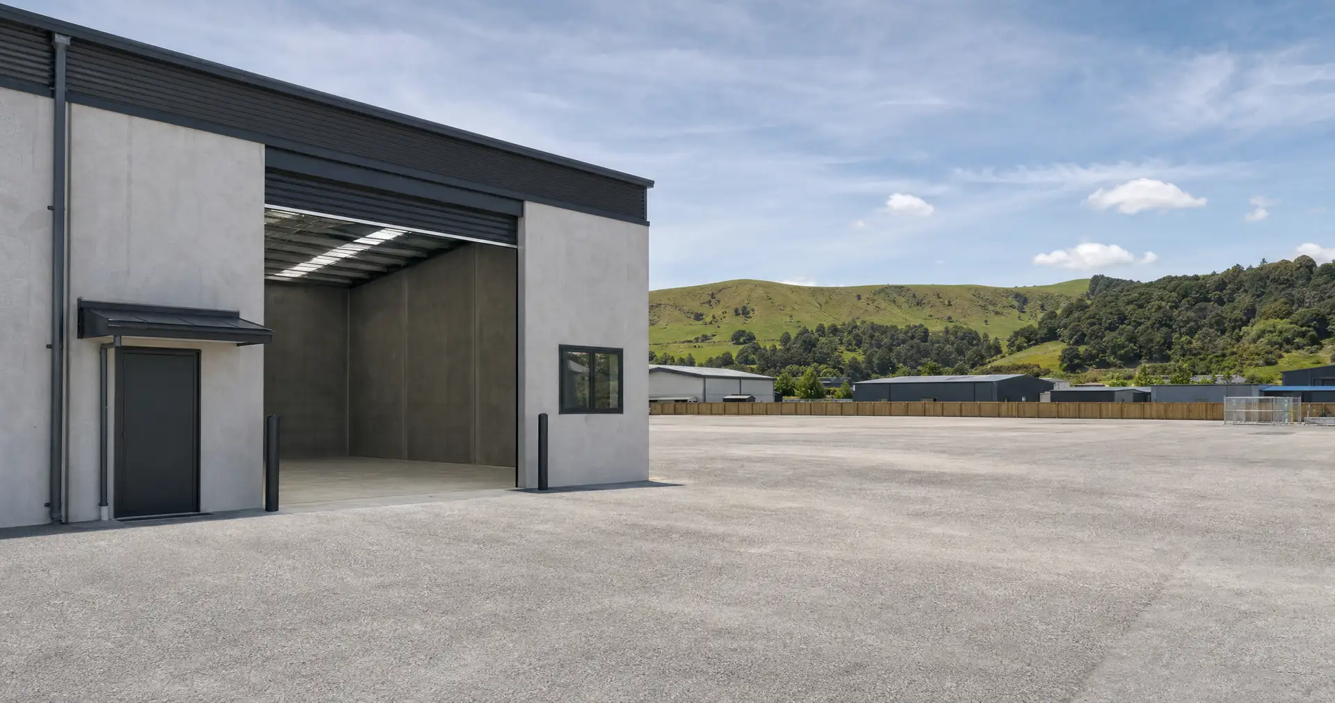 A tilt-slab light-industrial unit with its roller door up, seen across a sealed yard