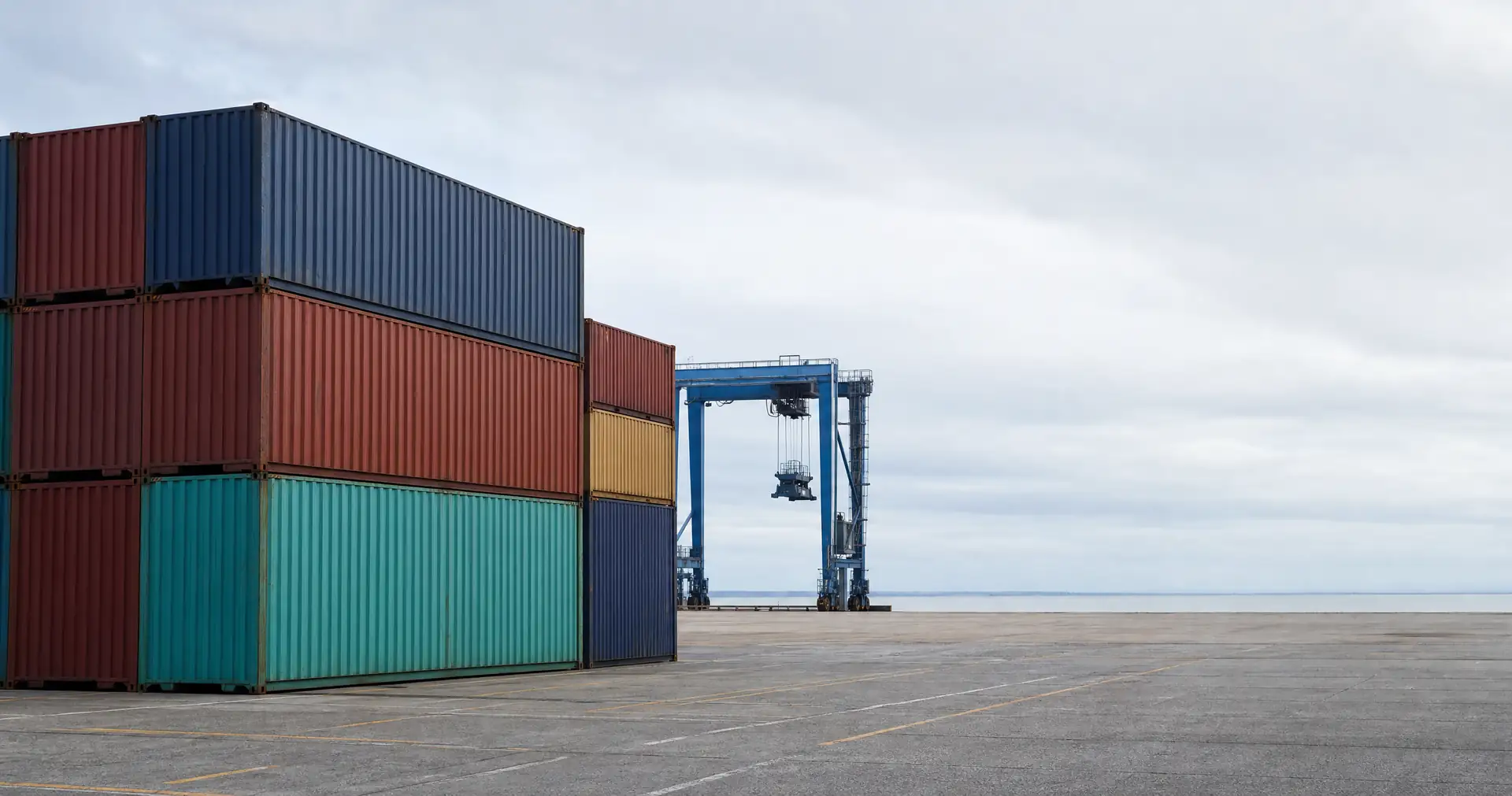 A stack of shipping containers in a port yard with a gantry crane behind