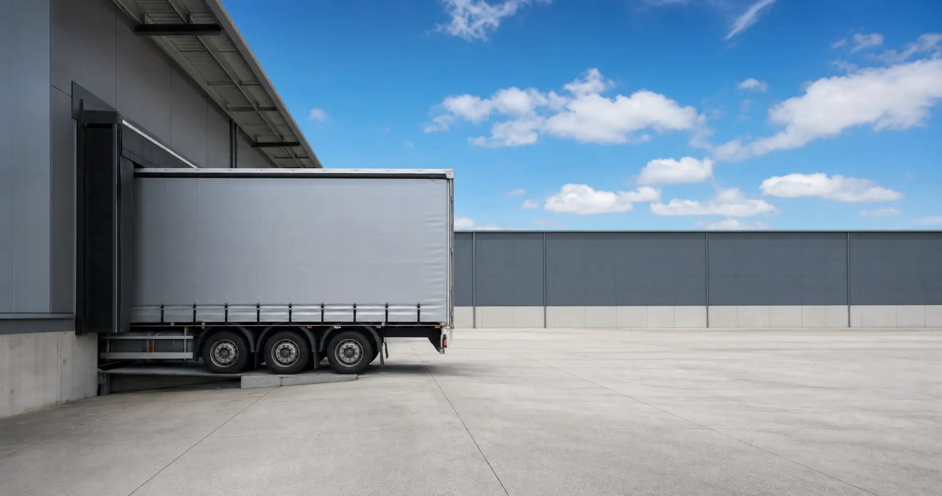 A curtainsider truck backed onto a raised loading dock at the side of a warehouse
